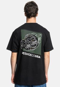 Black short-sleeve t-shirt featuring a graphic design with green grid pattern, white text "DC" and "DCSHOESUSA" on the back.