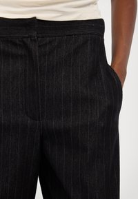 Svarte denimbukser med stripemotiv, utstyrt med frontlommer og en strukturert midjebånddesign.
