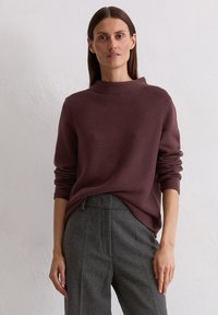 Burgundowy sweter dzianinowy z wysokim kołnierzem i długimi rękawami, zestawiony z ciemnoszarymi, dopasowanymi spodniami. Teksturowana tkanina i luźny krój.
