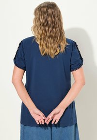 Námořnická modrá tričko s krátkými, nadýchanými rukávy. Obsahuje texturovaný lem podél okrajů rukávů. Měkký, bavlněný materiál a uvolněný střih.