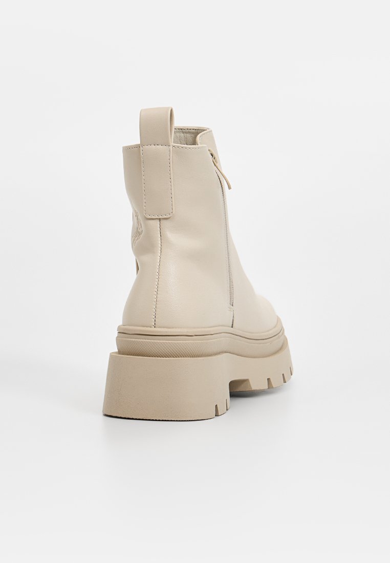 Beige Lederstiefeletten mit einer dicken Plattformsohle, ausgestattet mit einem Reißverschluss an der Rückseite und einem Schlaufen-Tab für einfaches An- und Ausziehen. Glatte Textur, minimales Design.