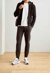 Black zip-up hoodie with ribbed texture, white t-shirt, dark gray tapered pants, and patterned white sneakers with accents.