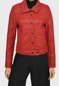 Červená kožená bunda s krátkým střihem, zapínáním na knoflíky a klopovým límcem. Má černé knoflíky a hladkou texturu.