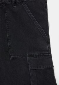 Pantalon en denim noir en gros plan montrant une poche avant diagonale et une poche cargo rectangulaire avec rabat sur le côté.
