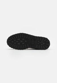 Black rubber shoe sole with deep treads, featuring triangular patterns and raised edges for traction. Textured surface for grip.