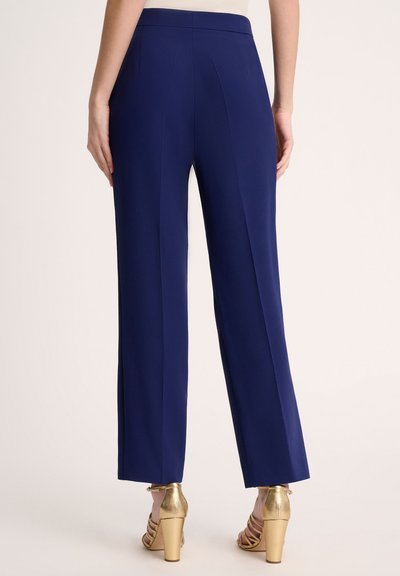 Navy wijde broek van gladde stof, met plooien aan de achterkant, gecombineerd met gouden hoge hakken.