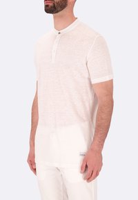 Polo shirt bianco a maniche corte realizzato in tessuto leggero e texture, con colletto bottonato e un sottile etichetta del marchio sull'orlo.