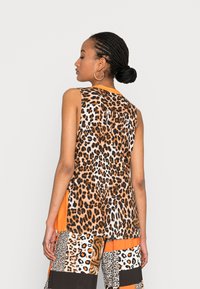 Top sem mangas com um design de padrão de leopardo, detalhes em laranja e um corte largo. O tecido tem uma textura suave com uma silhueta descontraída.