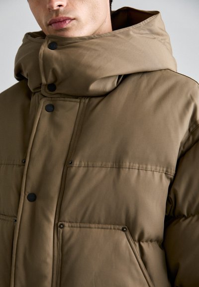 Khaki Steppjacke mit großer, strukturiertem Kapuze, Druckknöpfen und zwei Vordertaschen. Verfügt über eine glatte, matte Oberfläche.