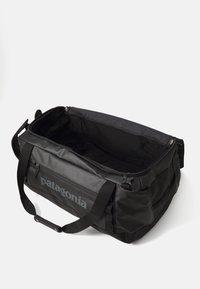 Black Patagonia duffel bag with open top, handles, front zippered pocket, and padded shoulder strap on white background.