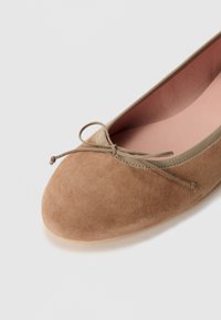 Ballerine in suede marrone con punta rotonda, decorate con un sottile fiocco e una morbida fodera interna in rosa chiaro in contrasto. Suola liscia.