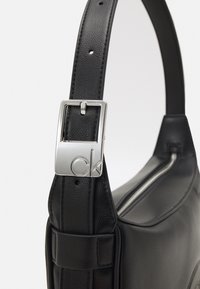 Czarna skórzana torba na ramię o teksturowanym wykończeniu i srebrnymi zapięciami. Posiada zamek błyskawiczny oraz regulowany pasek. Prosty, elegancki design.