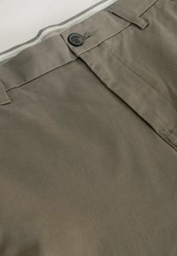 Tailored olive green pants with a smooth cotton fabric, featuring a metal button, subtle front crease, and contrasting waistband detail.