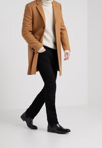 Tan wool overcoat, white cable-knit sweater, black fitted pants, and shiny black ankle boots. Simple design with solid colors.