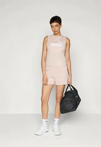 Svijetlo ružičasti top bez rukava s "PUMA" logotipom, usklađene kratke hlače, bijele tenisice i crna torba za teretanu. Glatka tkanina i sportski dizajn.