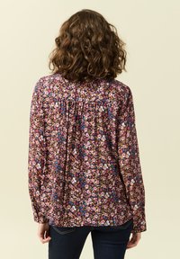 Blommig långärmad blus på mörk bakgrund med färgglada små blommor. Har inhägnad detaljer vid ryggen och knäppning vid ärmsluten.