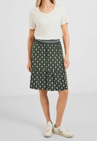 Baumwoll-T-Shirt in Hellbeige, kombiniert mit einem knieumspielenden, dunkelgrünen Rock mit Blumenmuster, der einen grauen elastischen Bund und ein gestuftes Design aufweist.