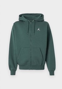 Felpa verde con zip realizzata in tessuto morbido, dotata di tasca frontale, cordini, polsini a coste e un piccolo logo bianco sul petto.