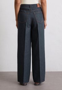 Szerokie, ciemnoniebieskie spodnie dżinsowe z wysokim stanem, z wyraźnymi zakładkami, dwiema tylnymi kieszeniami oraz kontrastowymi detalami szwów.