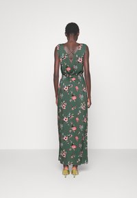 Blommig maxikjol i grönt tyg med röda och blå blommor. Har en V-back och korsettsdesign. Bärs med gula klacksandaler.