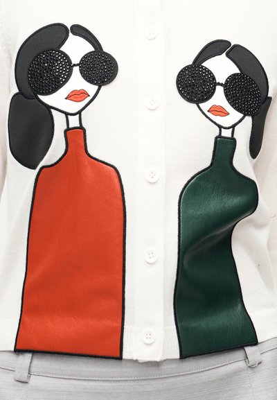 Bela jopica z dvema abstraknima figurama z sončnimi očali, ena v rdeči in druga v zeleni barvi, poudarjeni z usnjeno podobo.