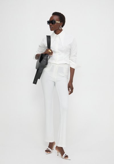 Chemise blanche sur mesure à col pointu, associée à un pantalon blanc évasé. Sac à main noir et lunettes de soleil surdimensionnées noires avec des accents dorés.
