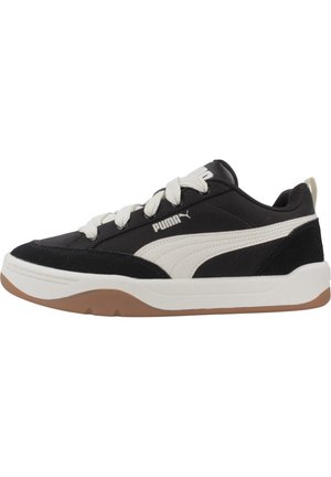 Sneaker bianco e nero con tessuto testurizzato, dettagli in suede e una suola in gomma marrone. Presenta lacci bianchi e un logo sul lato.