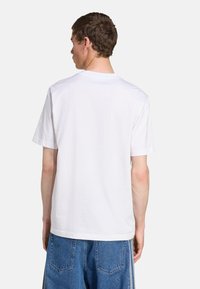 White cotton t-shirt with short sleeves and a crew neckline, featuring a plain texture. Worn with blue denim jeans in a relaxed fit.