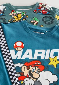 Kaksi sinistä graafista T-paitaa, joissa on Mario Kart -teemat. Toisessa paidassa on tummempi vihreä tausta ja hahmoja; toinen näyttää näyttävää "MARIO"-tekstiä ja sieniä.