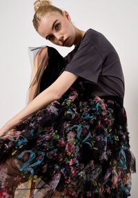 Czarna spódnica z tiulu z kolorowymi kwiatowymi wzorami, warstwowymi falbanami i niebieskimi akcentami, zestawiona z prostą ciemnoszarym topem z krótkim rękawem.