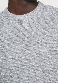 Grauer Strickpullover mit rundem Ausschnitt. Das strukturierte Gewebe zeigt ein dezentes Muster mit unterschiedlichen Maschen. Weiches, mittelgewichtiges Material.