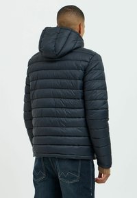 Sort pufferjakke med hætte, der har vandret syninger, en glat tekstur og et tætsiddende design, kombineret med mørke jeans.