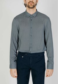 Camicia a maniche lunghe azzurro chiaro con motivo, con colletto button-down, abbinata a pantaloni blu scuro. La camicia presenta una stampa geometrica e una trama sottile.