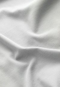 Světlá šedá textilní tkanina s jemným horizontálním žebrováním, vytvářející decentní vlnkový vzor. Materiál vypadá měkký a lehký.