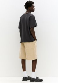 Tricou negru supradimensionat cu mâneci răsucite, pantaloni scurți kaki până la genunchi cu buzunare laterale, șosete albe și pantofi negri.