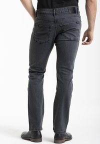 Jean en denim gris foncé avec une coupe droite, cinq poches et une finition texturée subtile. Portés avec des chaussures en cuir noires.