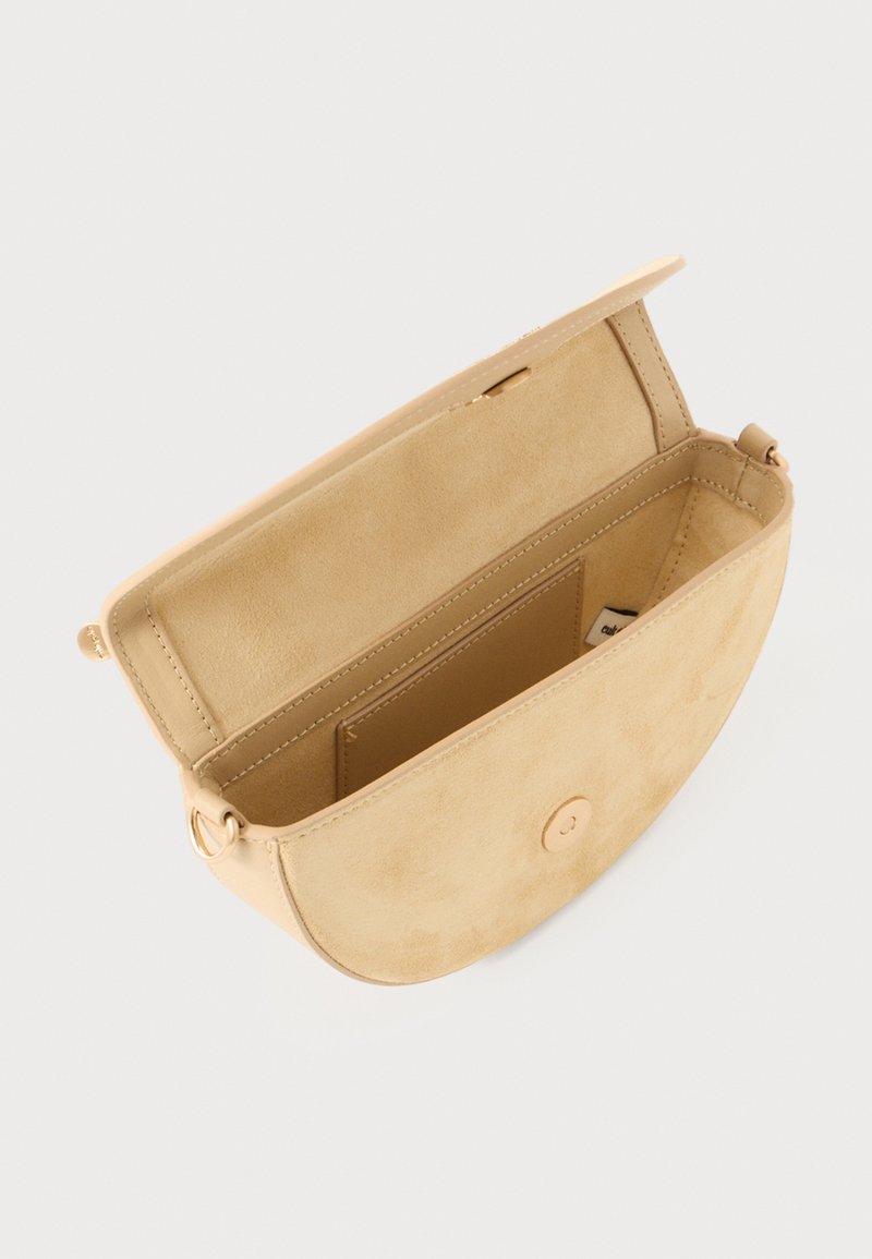 Beige, suede crossbody bag with a rounded shape, flap closure, and single interior compartment. Gold hardware details visible inside.