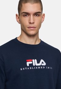 Felpa blu navy con scollatura rotonda e polsini a coste, con logo ricamato "FILA" e "ESTABLISHED 1911" in bianco e rosso.