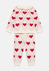 Pletený dvoudílný outfit v krémové barvě s červenými srdíčky, vybavený volánkovým límcem a žebrovanými manžetami. Sada obsahuje top s dlouhými rukávy a kalhoty.