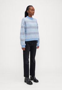 Sweater tricoté bleu clair avec motif géométrique, poignets et ourlet côtelés. Associé à un jean noir droité et des bottes à talons épais noires.