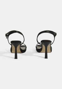 Schwarze High Heels Sandalen von hinten, mit einem schlanken Absatz, verstellbarem Knöchelriemen und Obermaterial aus weichem Stoff im minimalistischen Design.