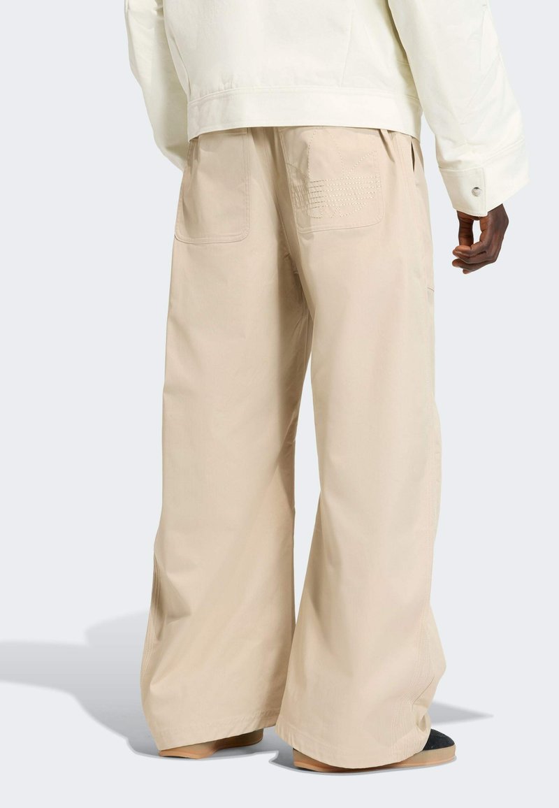 Beige wide-leg pants made of lightweight fabric, featuring two back pockets and subtle stitching details. Worn with a loose-fitting jacket.