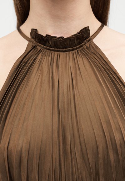 Gros plan sur une personne portant une robe marron plissée à col halter à volants, nouée autour du cou.