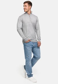 Suéter gris con cremallera y mangas largas, hecho de un tejido suave, combinado con unos jeans de mezclilla azul claro y zapatillas blancas.