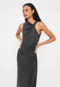 Tamno siva haljina bez rukava s dizajnom uvijenog čvora na ramenu, s drapiranim teksturom i prilagođenim siluetom koja se proteže do gležnjeva.