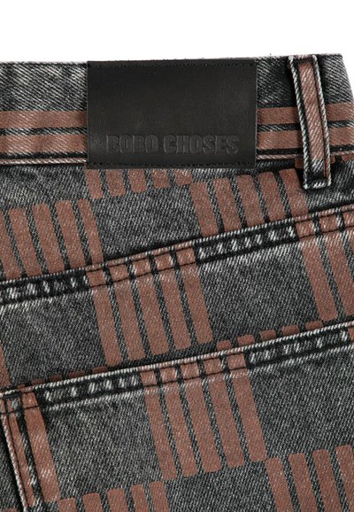 Gros plan d’un tissu en denim avec un motif à carreaux marron montrant une poche arrière et une étiquette en cuir noir embossée Bobo Choses.