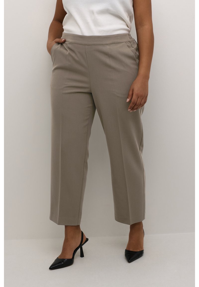 Beige, maßgeschneiderte Hosen mit hoher Taille und seitlichen Taschen. Gerades Bein-Design mit glatter Textur, kombiniert mit schwarzen Stilettos.