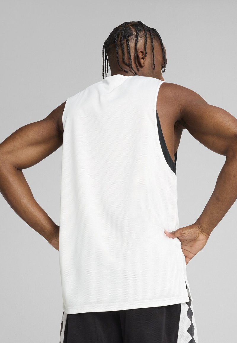 Camiseta atlética sin mangas blanca de tejido transpirable. Presenta un corte relajado, cuello redondo y una textura suave, llevada sobre pantalones cortos negros.