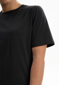 Schwarzes Baumwoll-T-Shirt mit Rundhalsausschnitt und kurzen Ärmeln. Der Stoff wirkt glatt, und der Schnitt ist bequem und lässig.