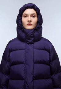 Fioletowa kurtka puchowa z dużym, regulowanym kapturem. Posiada pikowany wzór oraz elastyczny sznurek, zapewniający dopasowanie i ciepło.